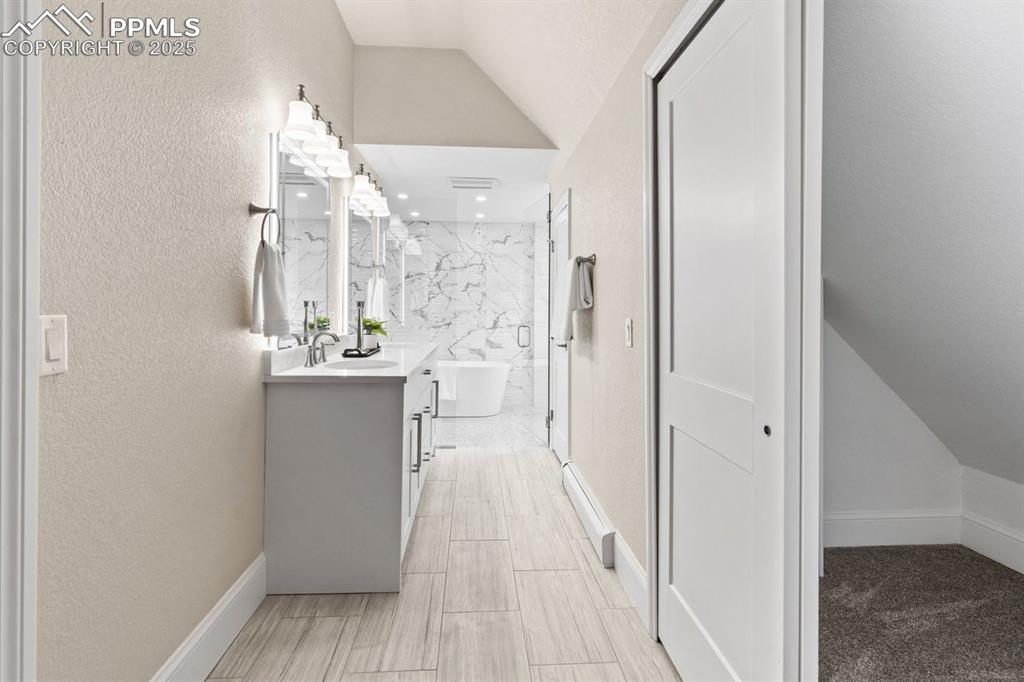Image 33 of 50: Bathroom with vanity, vaulted ceiling, a textured wall, a marble finish sho