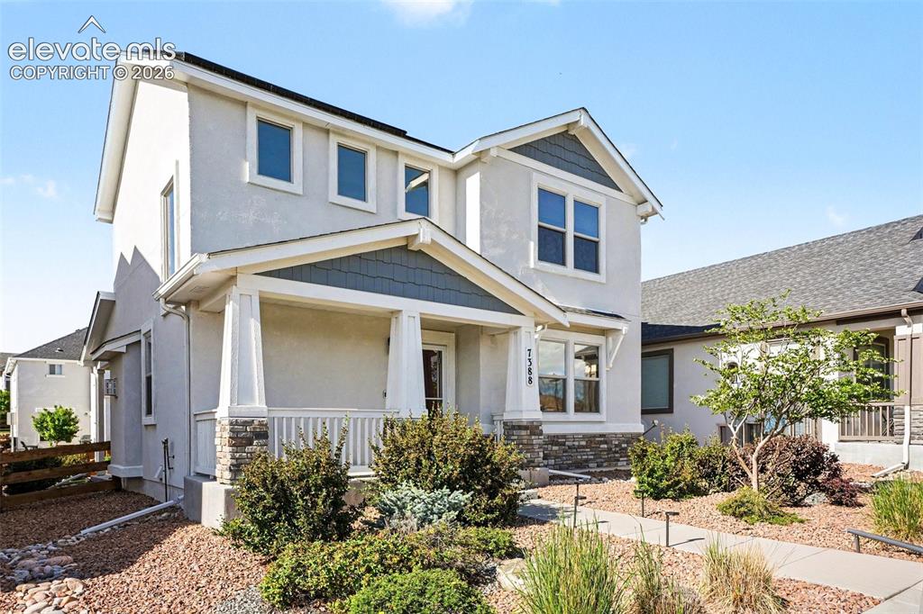Image 2 of 27: Two-story stucco home featuring a covered front porch with stone-clad colum
