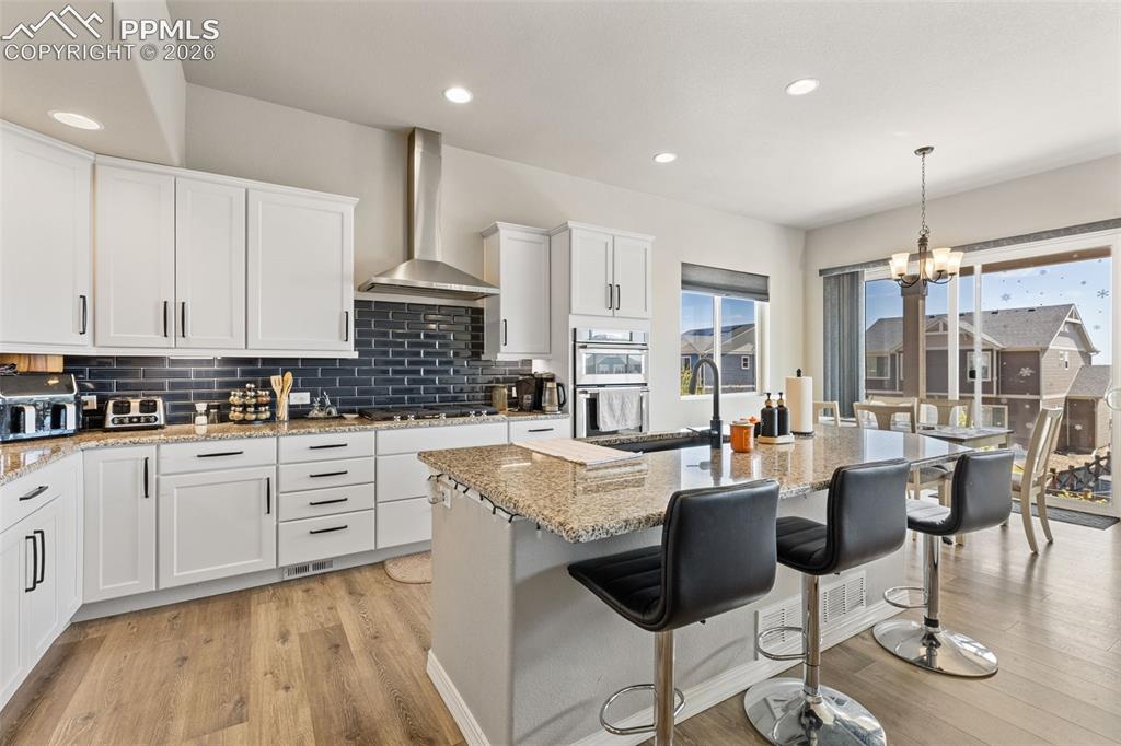 Image 17 of 44: Open-concept kitchen featuring white cabinetry, a dark subway tile backspla