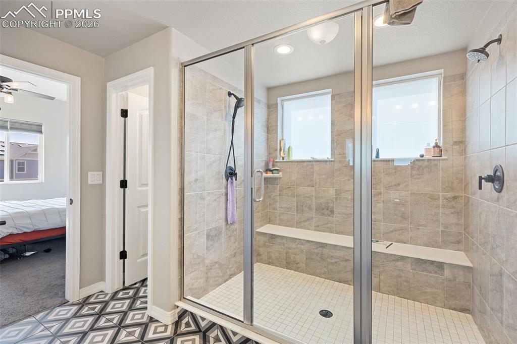 Image 29 of 44: Glass-enclosed shower featuring natural-toned tile walls, dual built-in ben