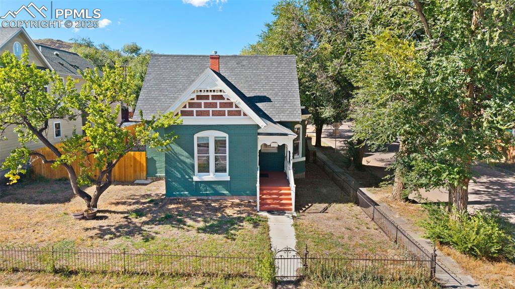 Image 30 of 36: View of front of home featuring a chimney, brick siding, a fenced front yar
