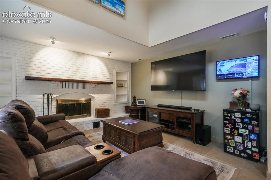 Image 24 of 50: Main level family room with gas fireplace, tile floors, built ins and acces