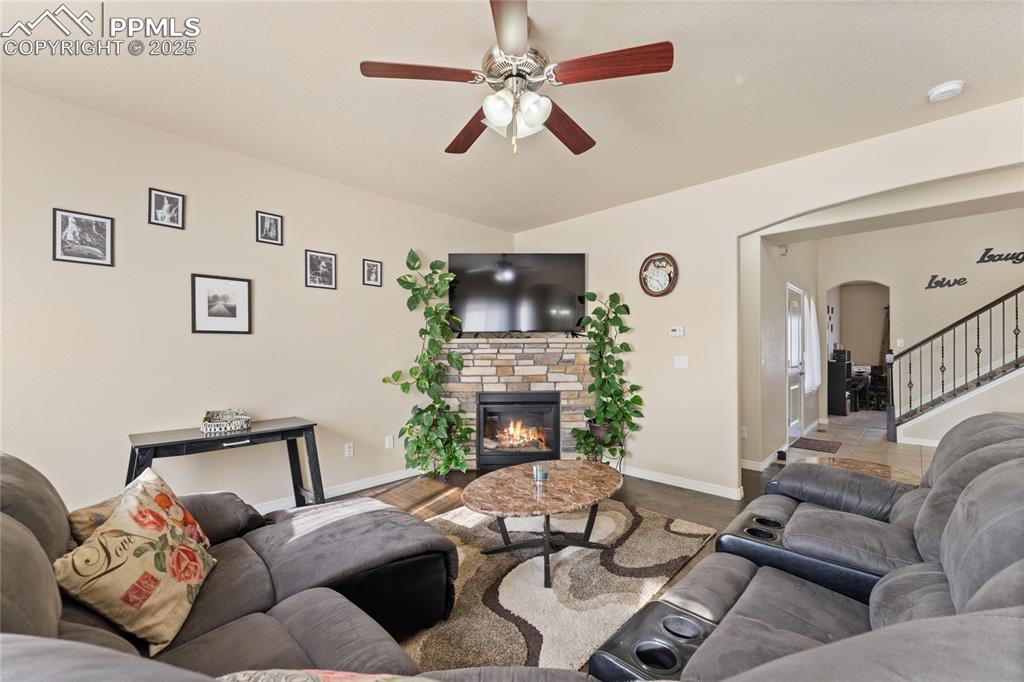 Image 8 of 38: Living room with arched walkways, wood floors, ceiling fan and gas fireplac