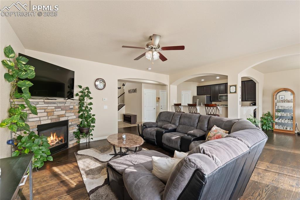 Image 9 of 38: Living room with arched walkways, wood floors, ceiling fan and gas fireplac