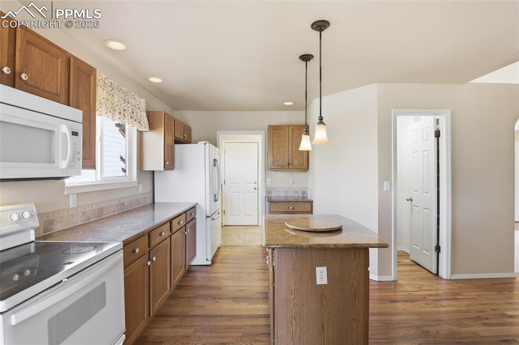 Image 26 of 50: Kitchen featuring white appliances, wood finish cabinetry, and dark wood-st