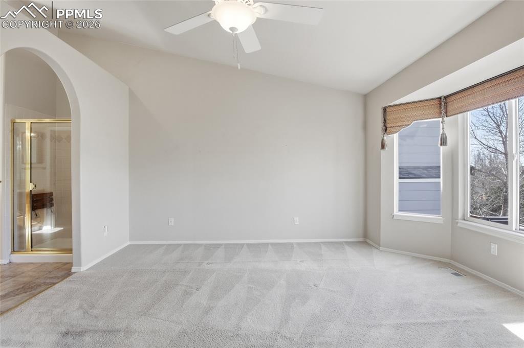 Image 32 of 50: Spare room featuring light carpet, ceiling fan, and arched walkways
