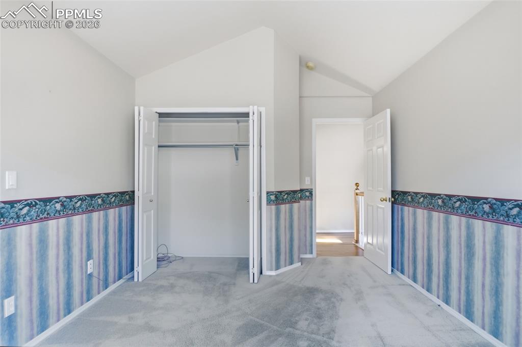 Image 38 of 50: Unfurnished bedroom with wallpapered walls, wainscoting, lofted ceiling, li