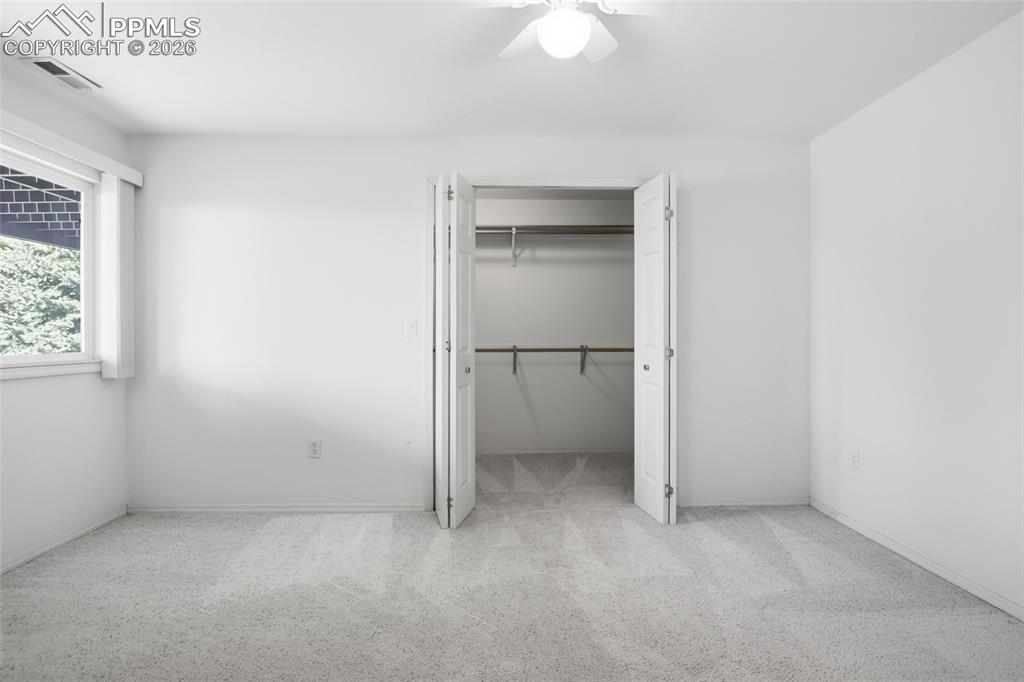 Image 46 of 50: Unfurnished bedroom with light carpet, a walk in closet, and a ceiling fan