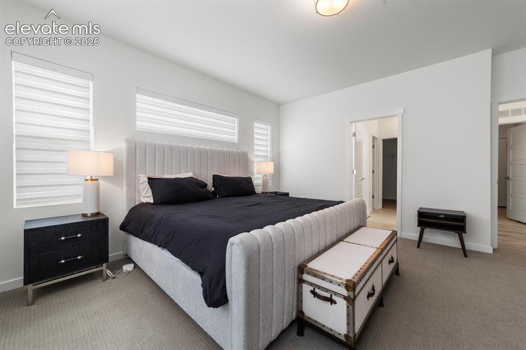 Image 24 of 38: Spacious bedroom featuring white walls, light-colored carpet, and multiple
