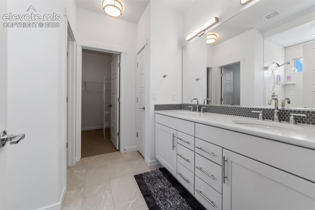 Image 25 of 38: Bathroom featuring a double vanity with white cabinetry, dual undermount si
