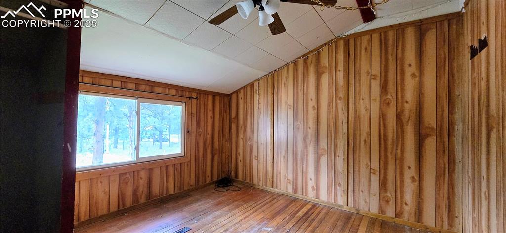 Image 30 of 48: Spare room with hardwood / wood-style flooring, wood walls, ceiling fan, an