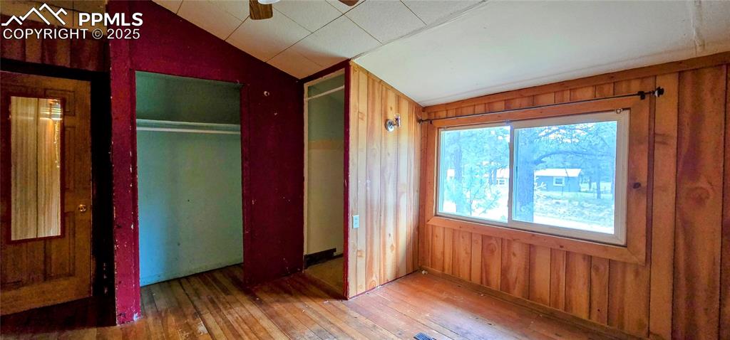 Image 31 of 48: Unfurnished bedroom with lofted ceiling, wood walls, hardwood / wood-style 