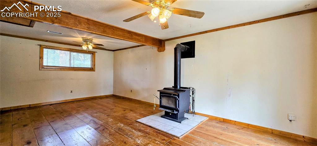 Image 39 of 48: Unfurnished living room with a wood stove, wood-type flooring, beam ceiling