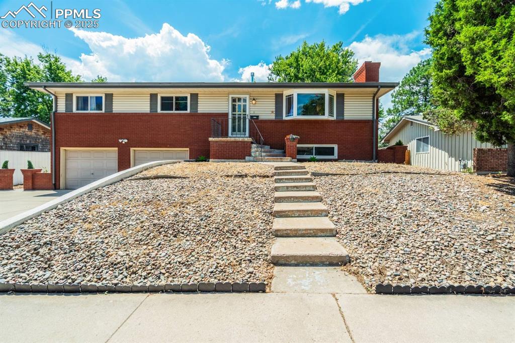 Caption: Ranch-style house featuring brick siding, a chimney, an attached garage, and driveway