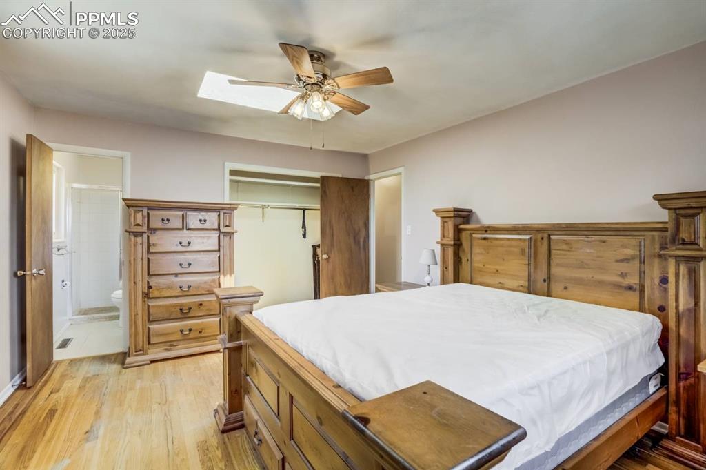 Image 14 of 37: Bedroom with a skylight, light wood-type flooring, connected bathroom, a cl