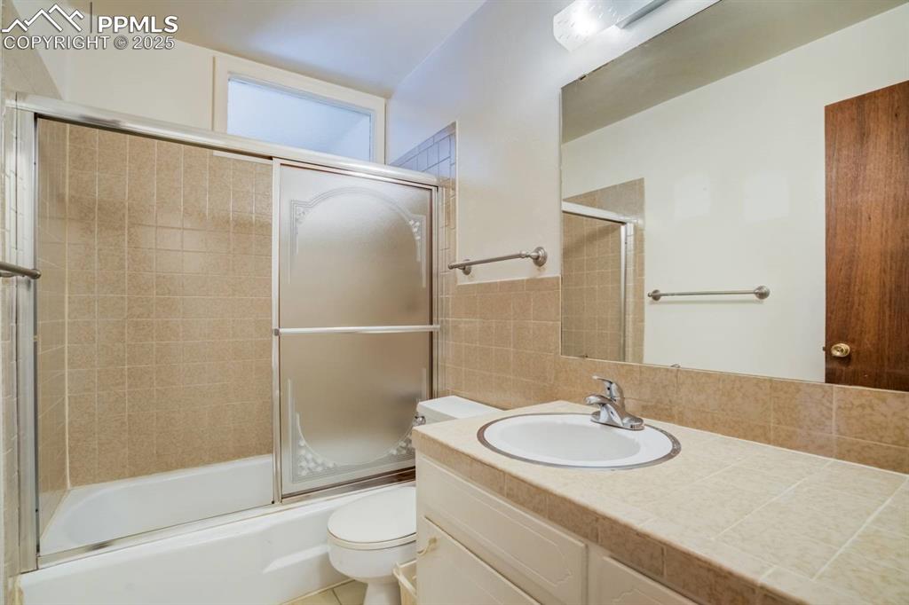 Image 18 of 37: Full bath with vanity, bath / shower combo with glass door, and tile walls