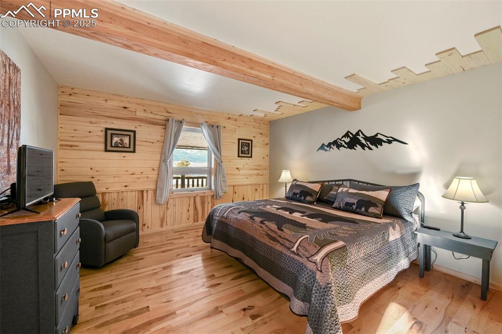 Image 28 of 50: Bedroom with baseboards, beamed ceiling, wooden walls, and light wood-type