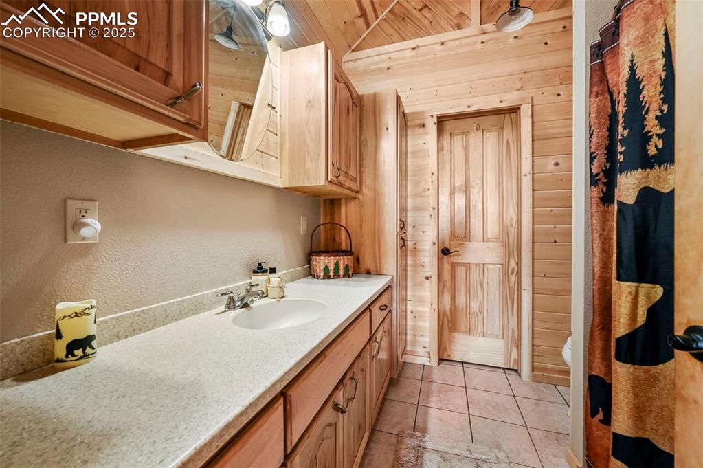 Image 40 of 50: Bathroom with tile patterned floors, wooden walls, wooden ceiling, and vani