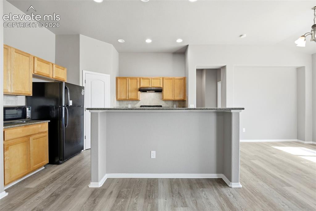 Image 11 of 31: Kitchen featuring wood-finish cabinetry, black appliances, light-toned back