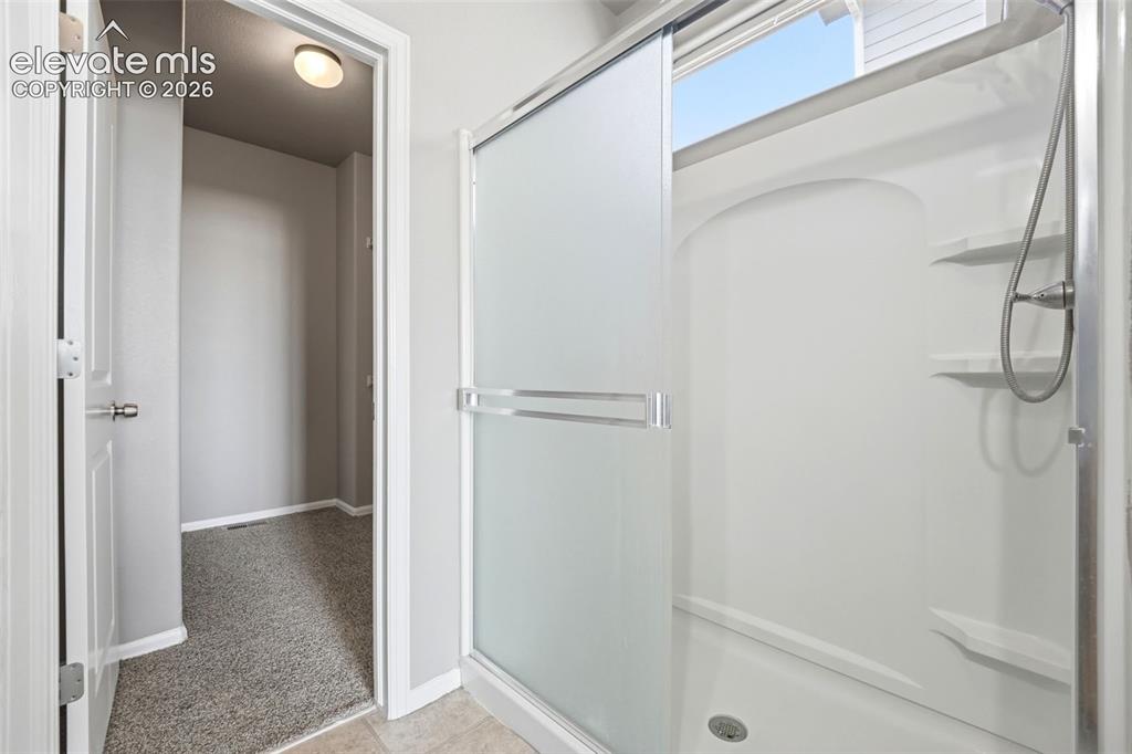 Image 19 of 31: Shower with a sliding frosted glass door, integrated shelving, and a chrome