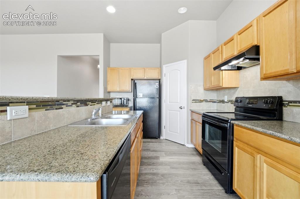 Image 5 of 31: Kitchen with light wood cabinetry, stone-finish countertops, and a tiled ba
