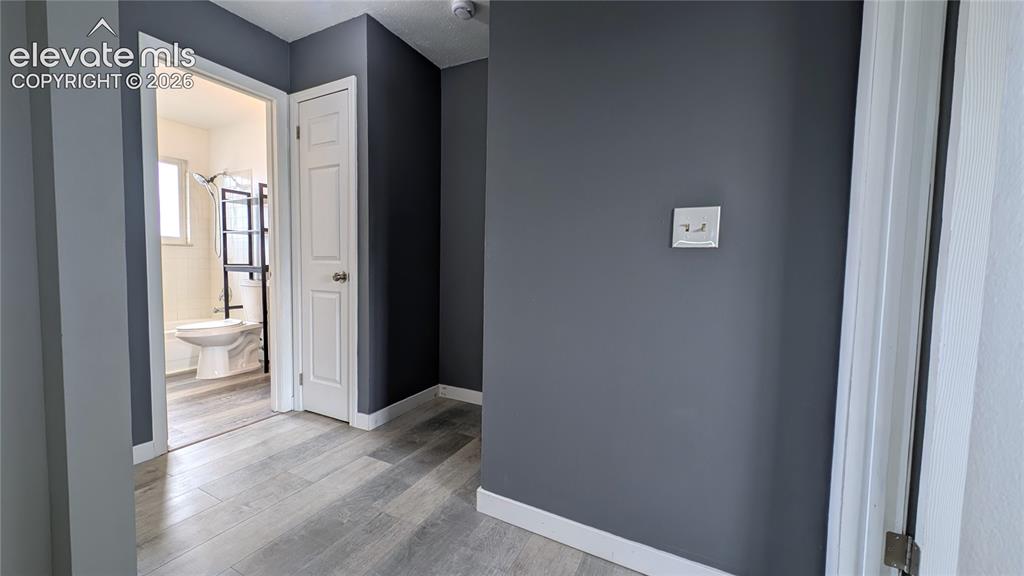Image 20 of 24: Hallway with light wood-finish flooring, dark gray walls, and white baseboa