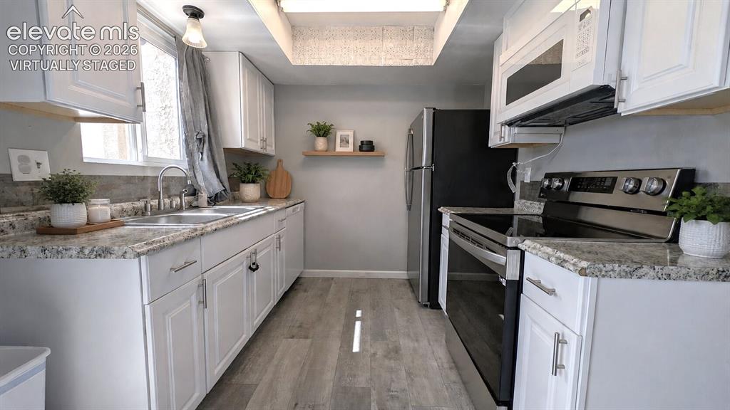 Image 4 of 24: Galley kitchen featuring white cabinetry, granite-finish countertops, stain
