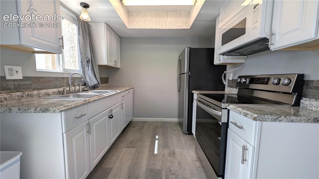 Image 5 of 24: Kitchen featuring white cabinetry, wood-finish flooring, and a skylight