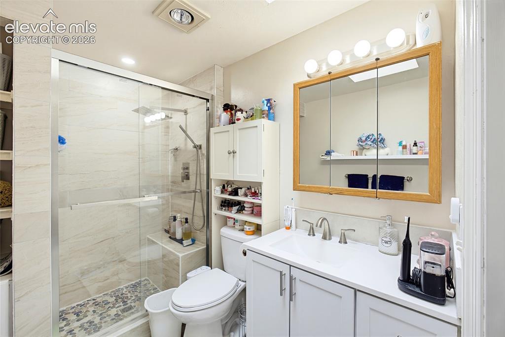 Image 29 of 32: Glass-enclosed shower with stone tile surround and built-in bench