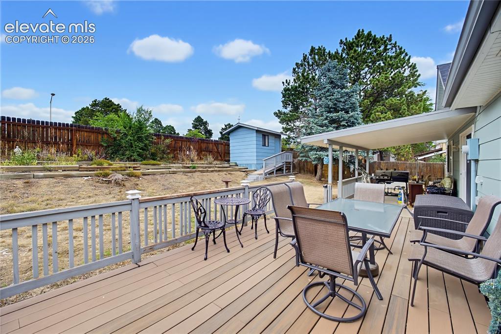 Image 8 of 32: Expansive wood-finish deck with a solid railing, covered patio area, and a 