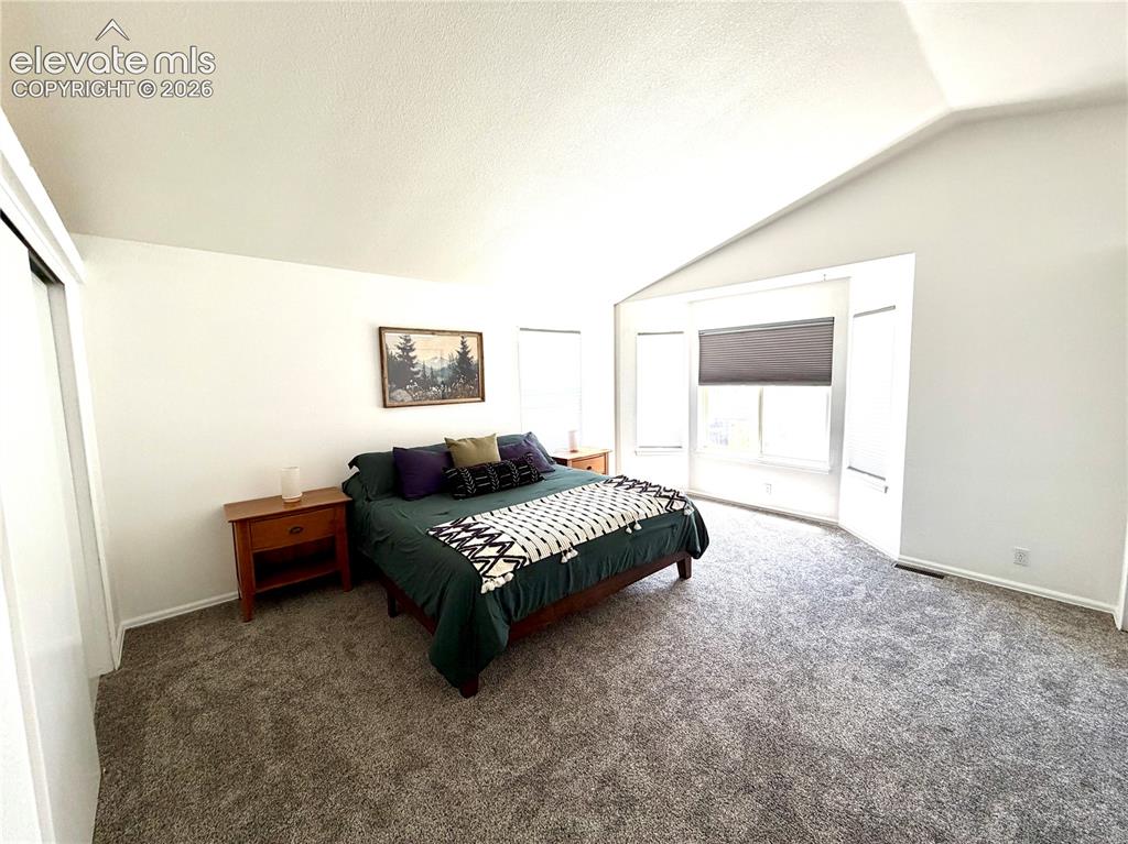 Image 13 of 50: Carpeted room featuring a vaulted ceiling, light-colored walls, and a bay w