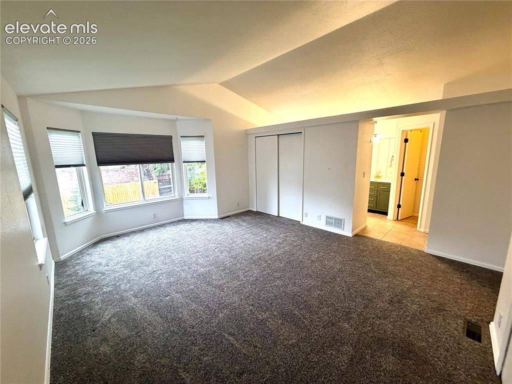 Image 16 of 50: Carpeted room featuring a bay window with blinds, vaulted ceiling, and slid