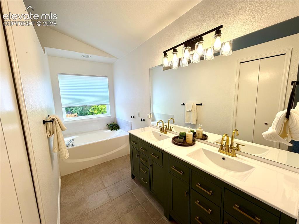 Image 17 of 50: Double vanity with green cabinetry and gold-finish fixtures, a large mirror