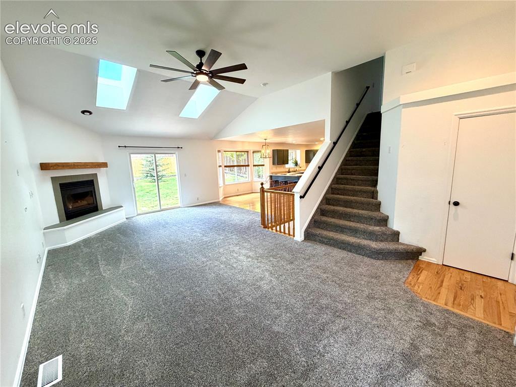 Image 4 of 50: Vaulted living room featuring a corner fireplace with a wood mantle, two sk