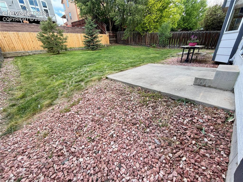 Image 44 of 50: Spacious backyard with a large lawn area, trees, and a concrete patio