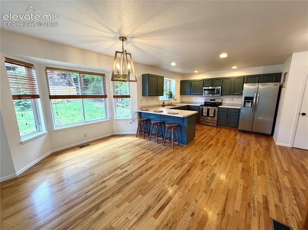 Image 7 of 50: Open-concept kitchen and dining area featuring wood-finish flooring, a bay