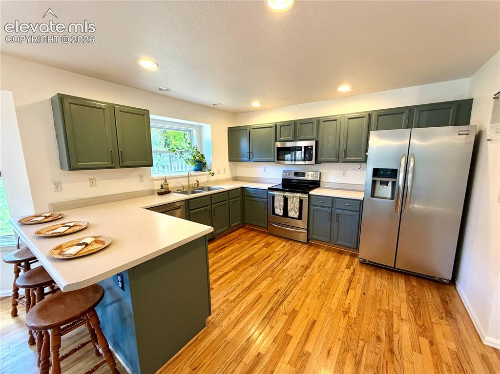 Image 8 of 50: Kitchen featuring a breakfast bar, wood-finish flooring, dark green cabinet