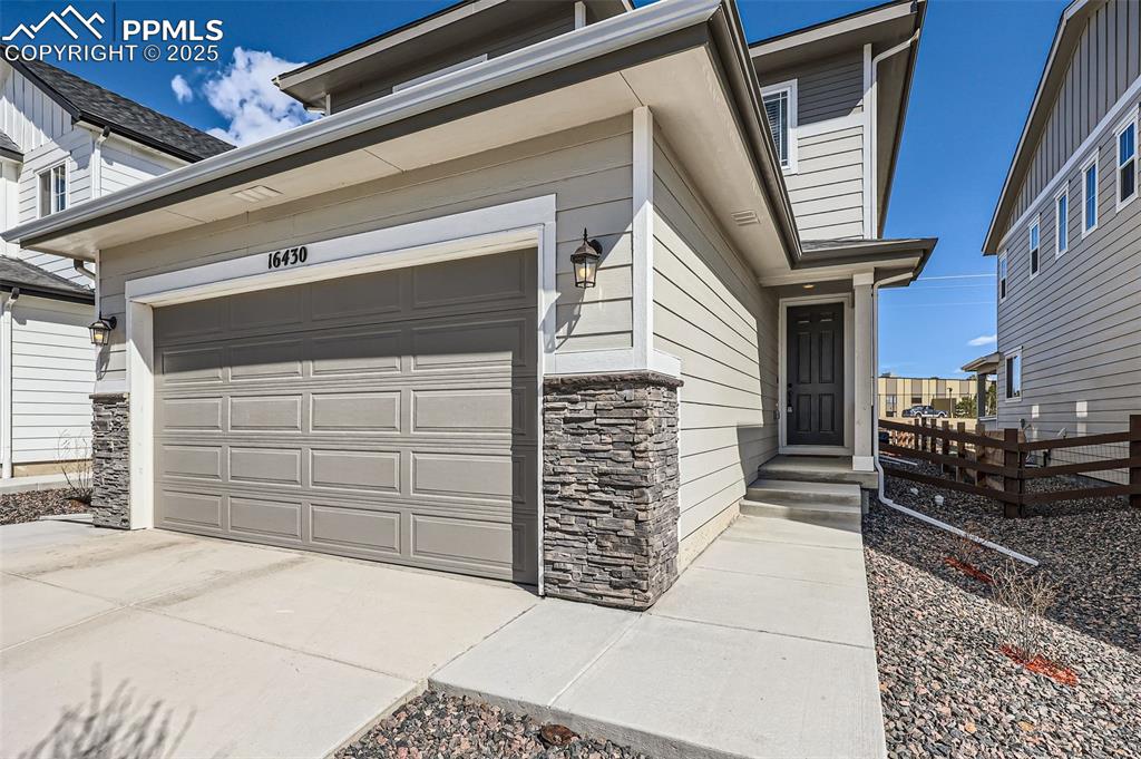 Image 3 of 27: View of front of property featuring a garage, stone siding, concrete drivew