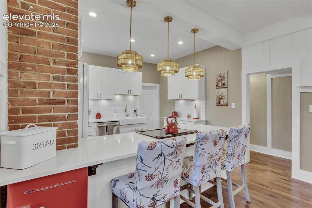 Image 12 of 43: Open-concept kitchen featuring an exposed brick pillar, white shaker cabine