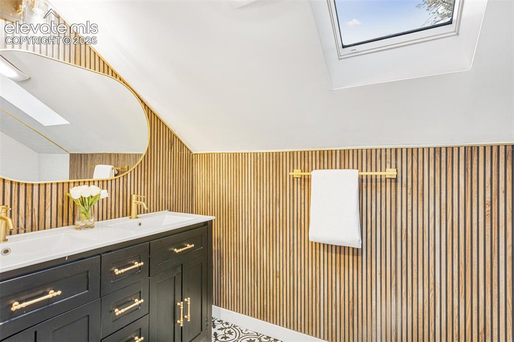 Image 22 of 43: Bathroom featuring a dual-sink vanity with black cabinetry and gold-tone ha