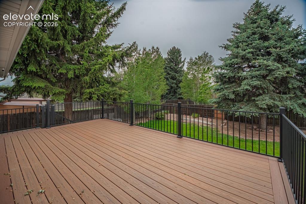 Image 28 of 34: Spacious composite deck with black metal railings overlooking a backyard wi