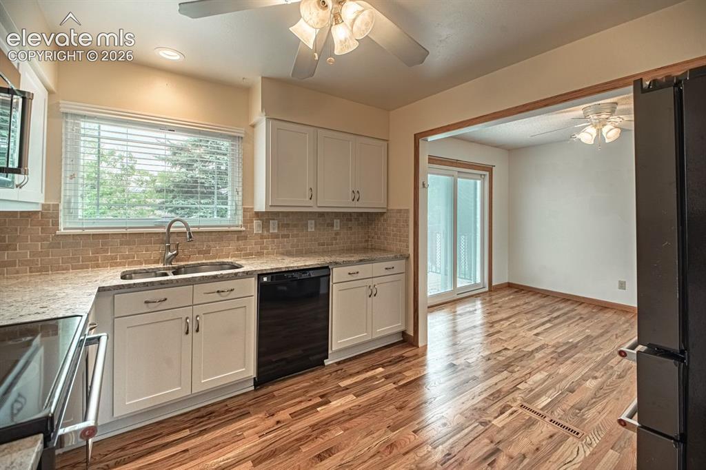 Image 4 of 34: Kitchen featuring hardwood flooring, white cabinetry, integrated black appl