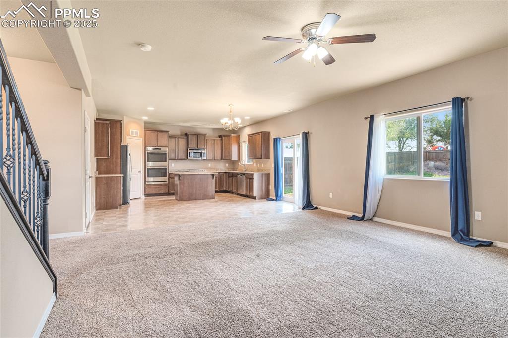 Image 11 of 43: Unfurnished living room featuring a chandelier, light colored carpet, stair