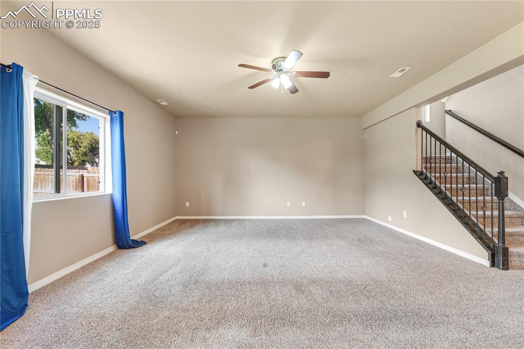 Image 14 of 43: Spare room featuring stairway, carpet flooring, and a ceiling fan