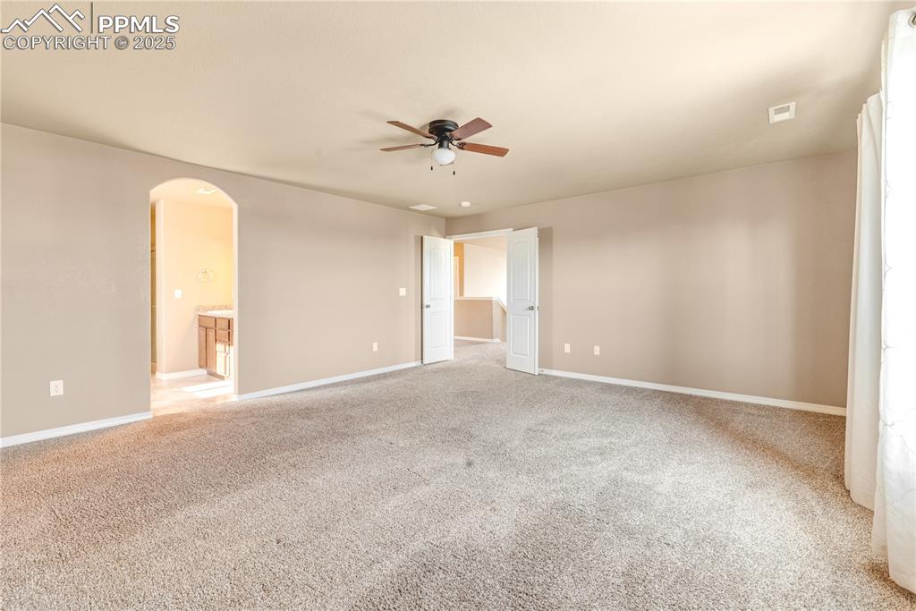Image 19 of 43: Unfurnished room with carpet, arched walkways, and a ceiling fan