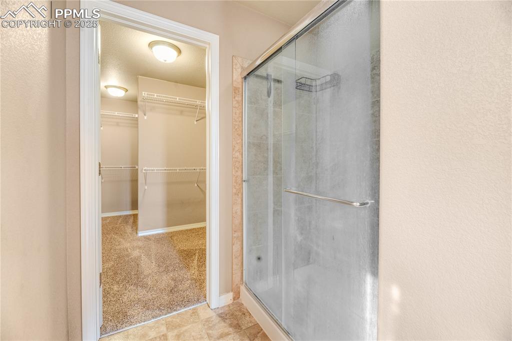Image 23 of 43: Full bathroom featuring a stall shower, a spacious closet, and a textured w