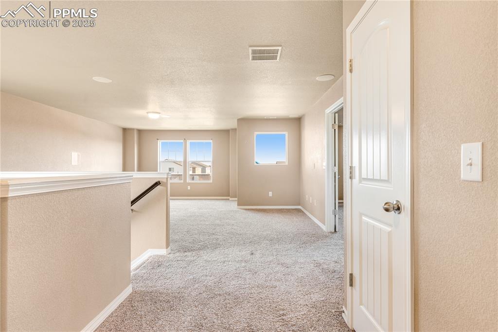 Image 31 of 43: Corridor with an upstairs landing, light colored carpet, a textured ceiling