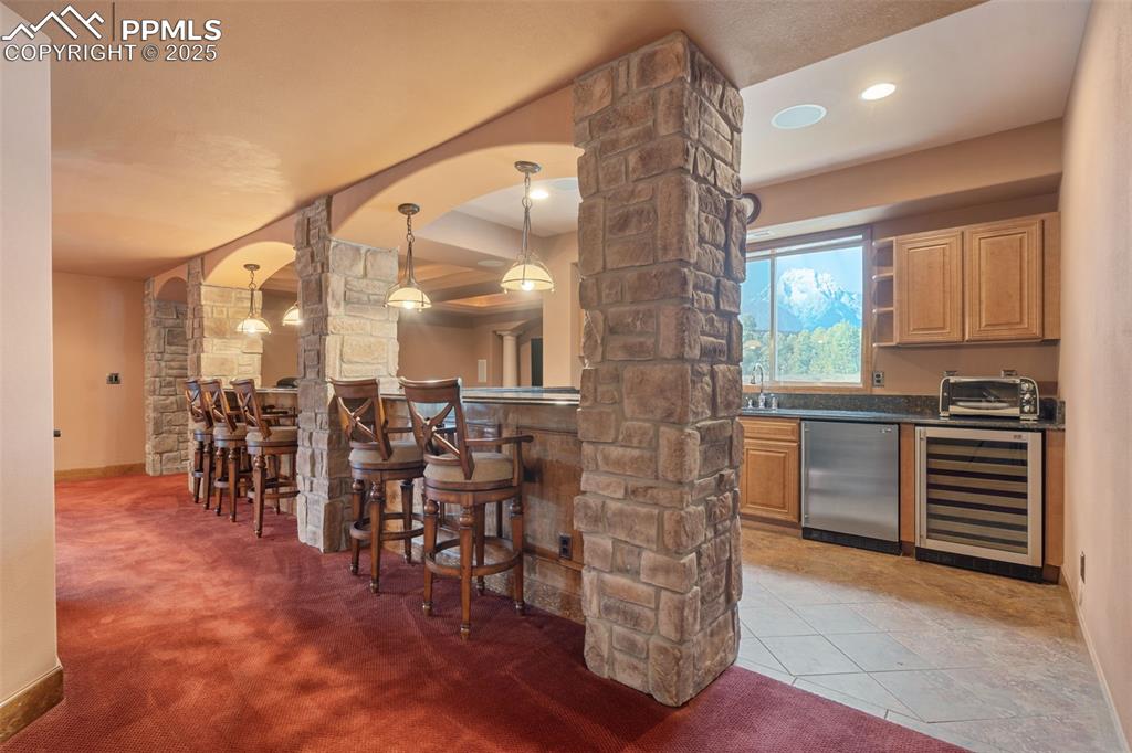 Image 32 of 50: Indoor wet bar featuring beverage cooler, decorative columns, arched walkwa