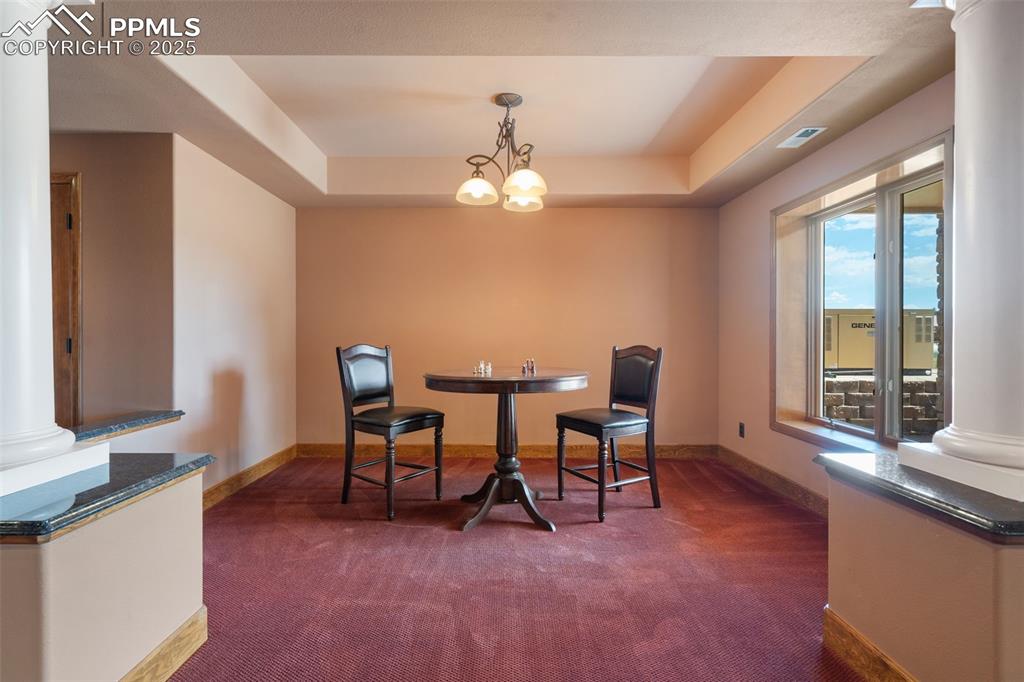 Image 34 of 50: Dining space with dark carpet, decorative columns, a raised ceiling, and a 