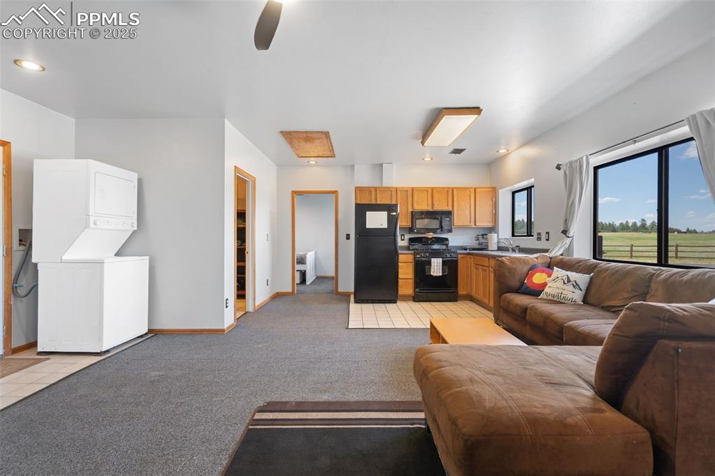Image 47 of 50: Living area with estacked washer and dryer, light carpet, ceiling fan, and 